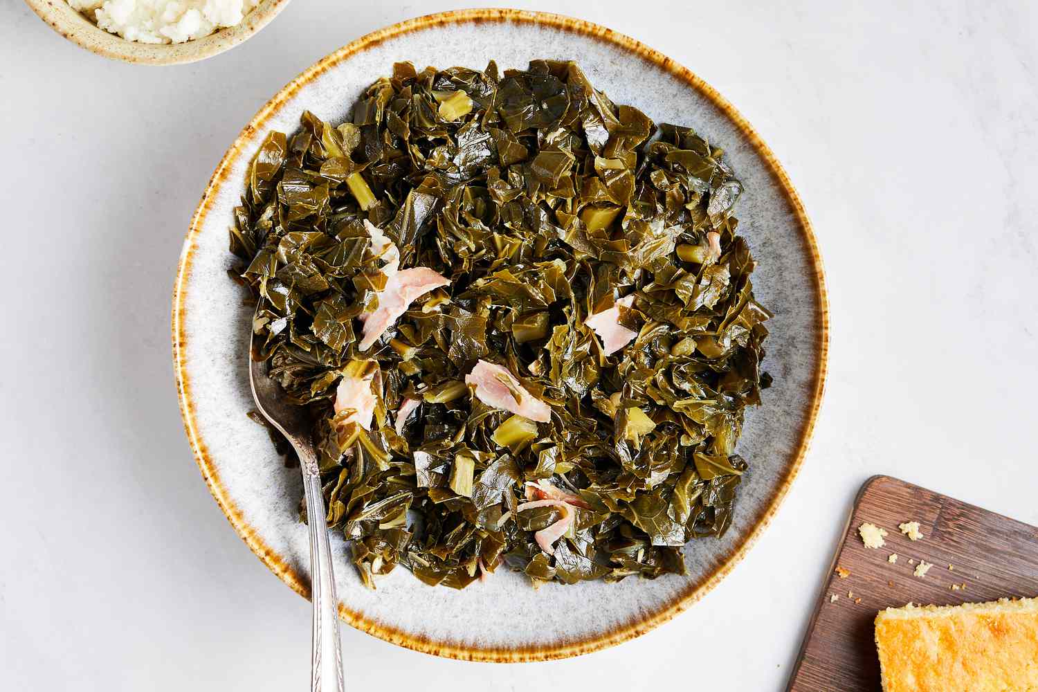 Instant Pot Collard Greens on a Plate with Serving Utensil Next to a Bowl of Mashed Potatoes and Cornbread