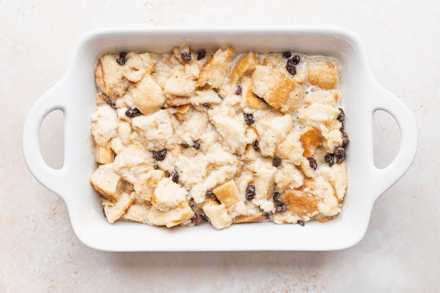 A white casserole dish with bread pudding ready to be baked