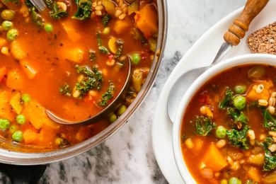 A pot and a bowl of vegetable soup with a ladle bread on the plate beside the bowl