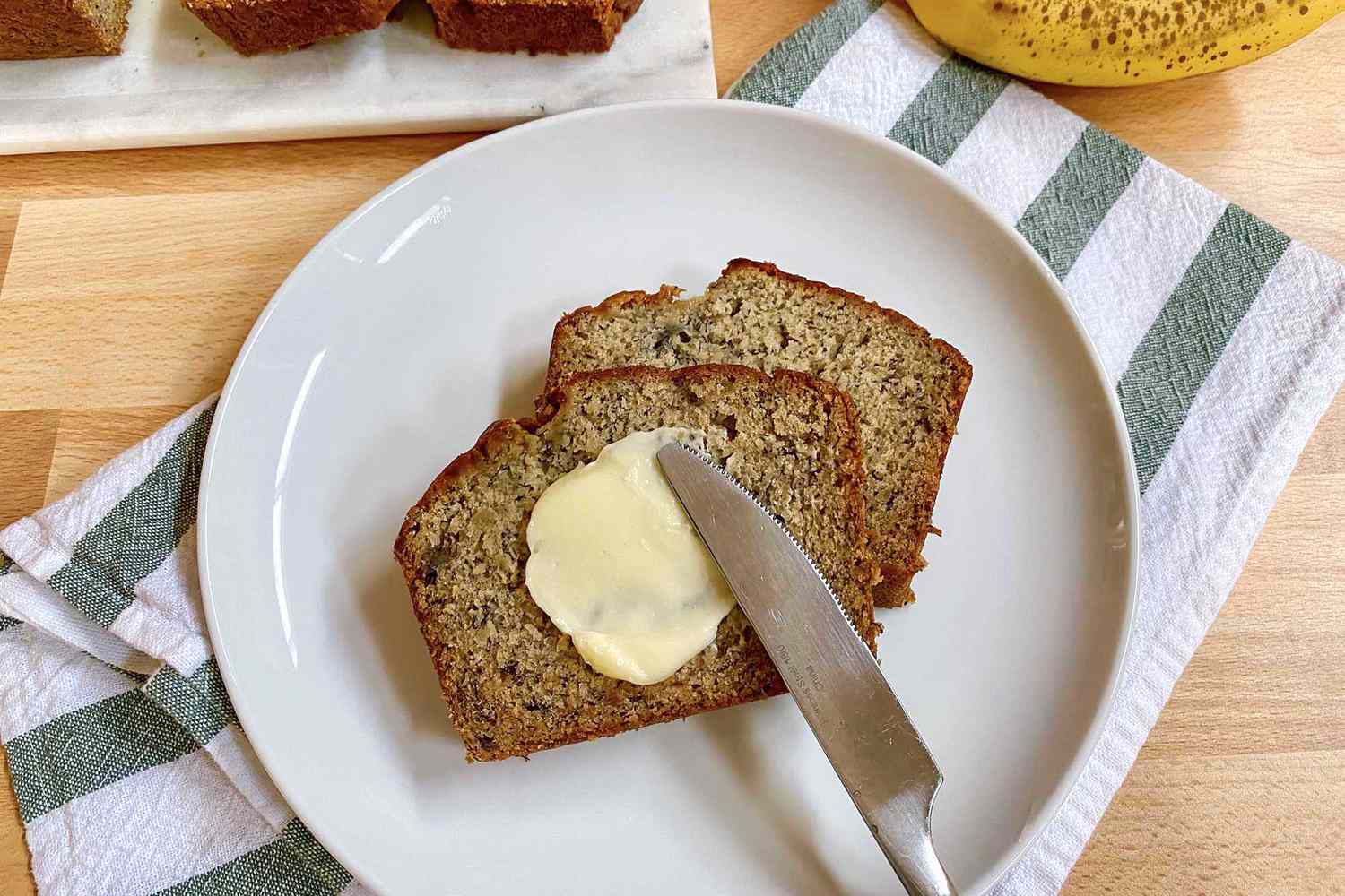 Two slices of easy gluten free banana bread with a pat of butter being spread on top.