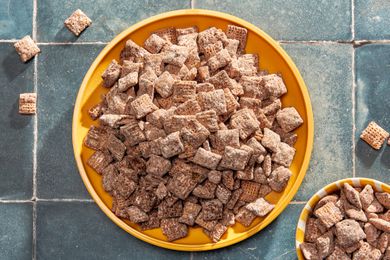 Bowl of nutella puppy chow next to a smaller bowl with more on a counter with some pieces of puppy chow scattered around