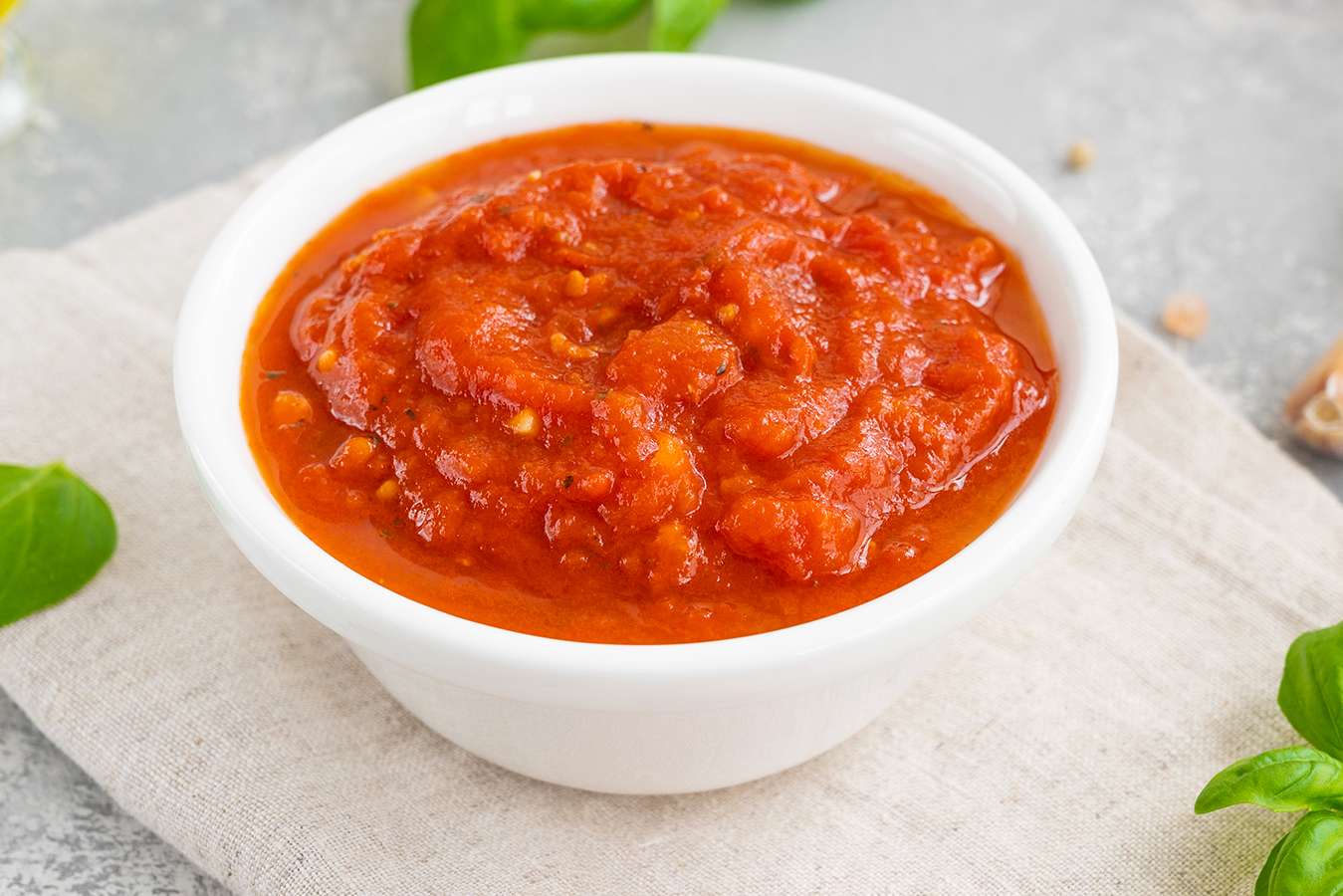 A small white dish with tomatobased sauce placed on a neutral background and garnished with herbs