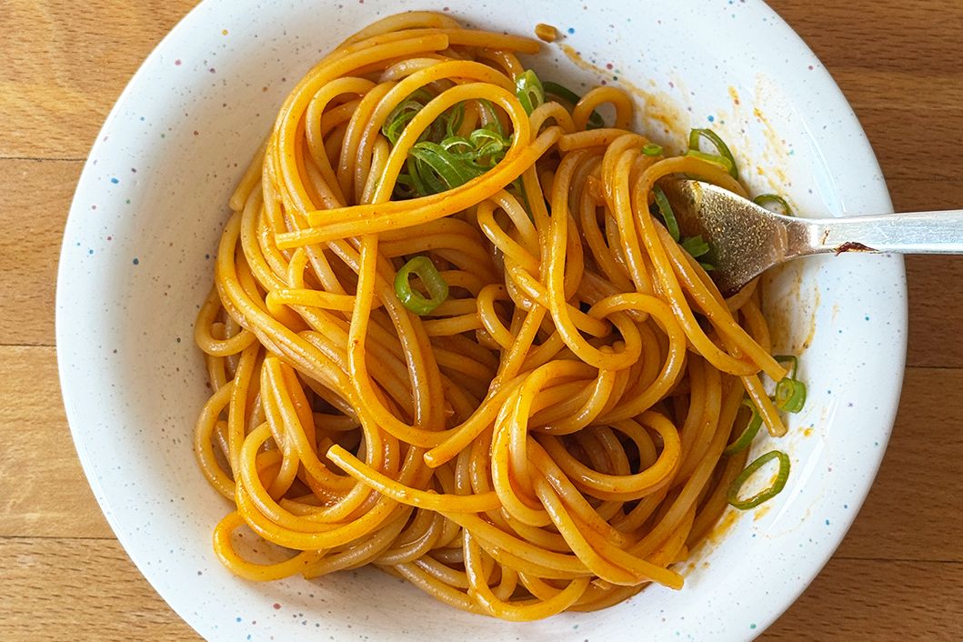 Bowl of cooked noodles garnished with green onions and a fork resting on the side