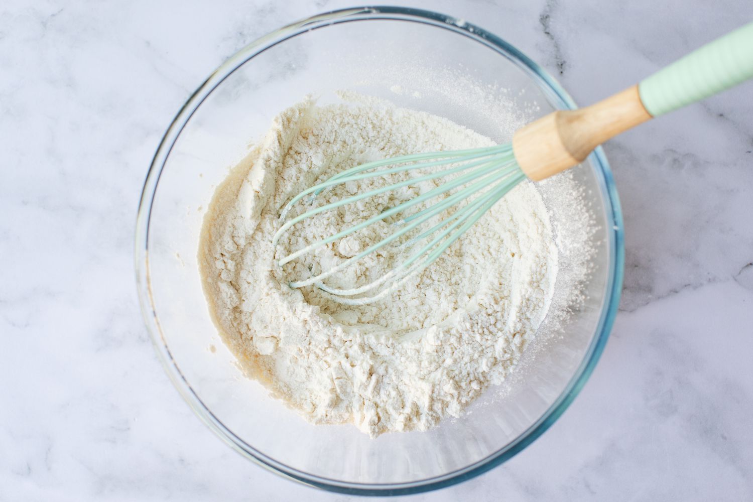 Flour and baking soda whisked in a glass bowl to make a Banana Nut Muffin recipe