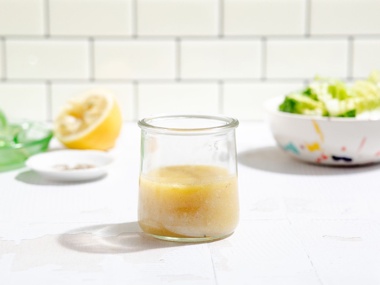 Salad dressing in a small glass jar with a salad in the background