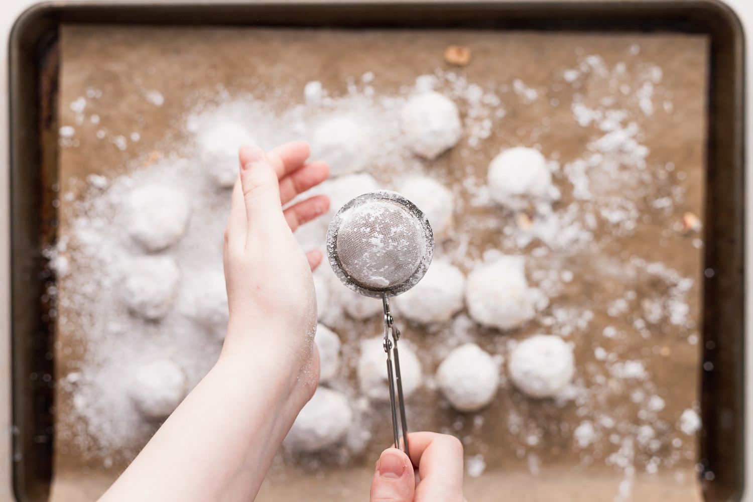 Dusting powdered sugar cookies with powdered sugar.