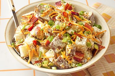 A bowl filled with loaded potato salad garnished with cheese scallions and bacon