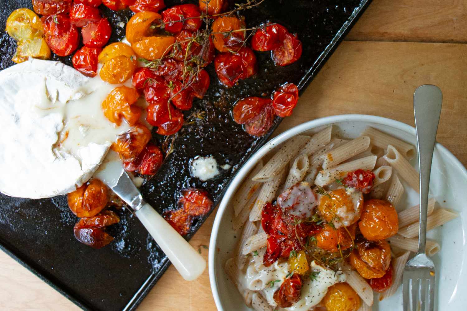 Cooked tomatoes served over pasta on a plate, with roasted tomatoes on a tray nearby