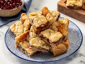 Side view of 2-ingredient jam bar squares piled high on a blue and white plate, with a bowl of jam in the background
