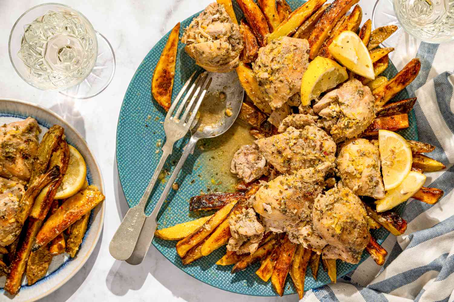 A plate of braised chicken with fried potatoes and lemon wedges on a blue platter