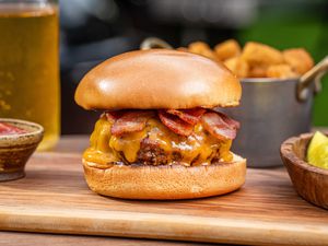 Best bacon cheeseburger set on a wood board outside.