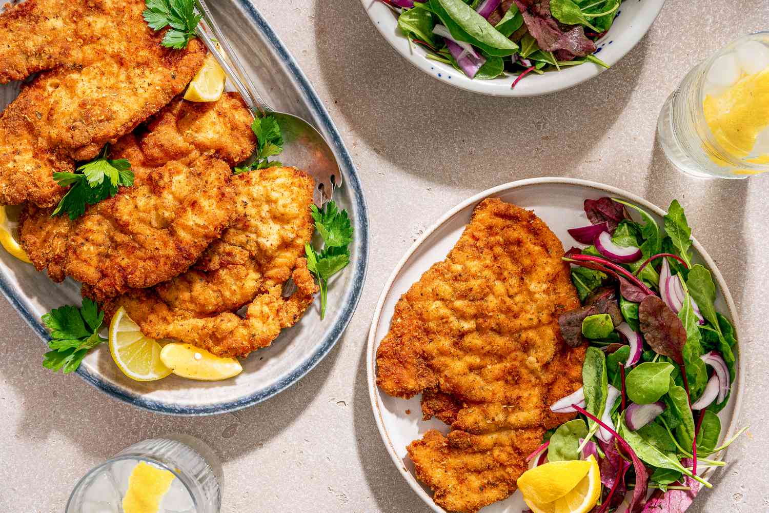 Chicken Romano on a platter, one piece of chicken on a plate with a side salad of mixed greens, two glasses of ice water with lemon 