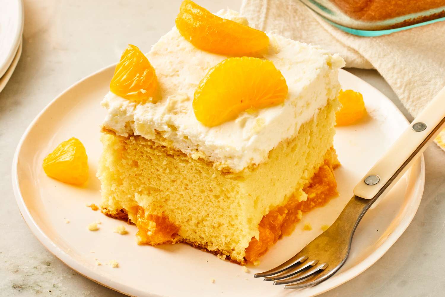 Angled view of a slice of pineapple and mandarin orange cake on a dessert plate with a fork
