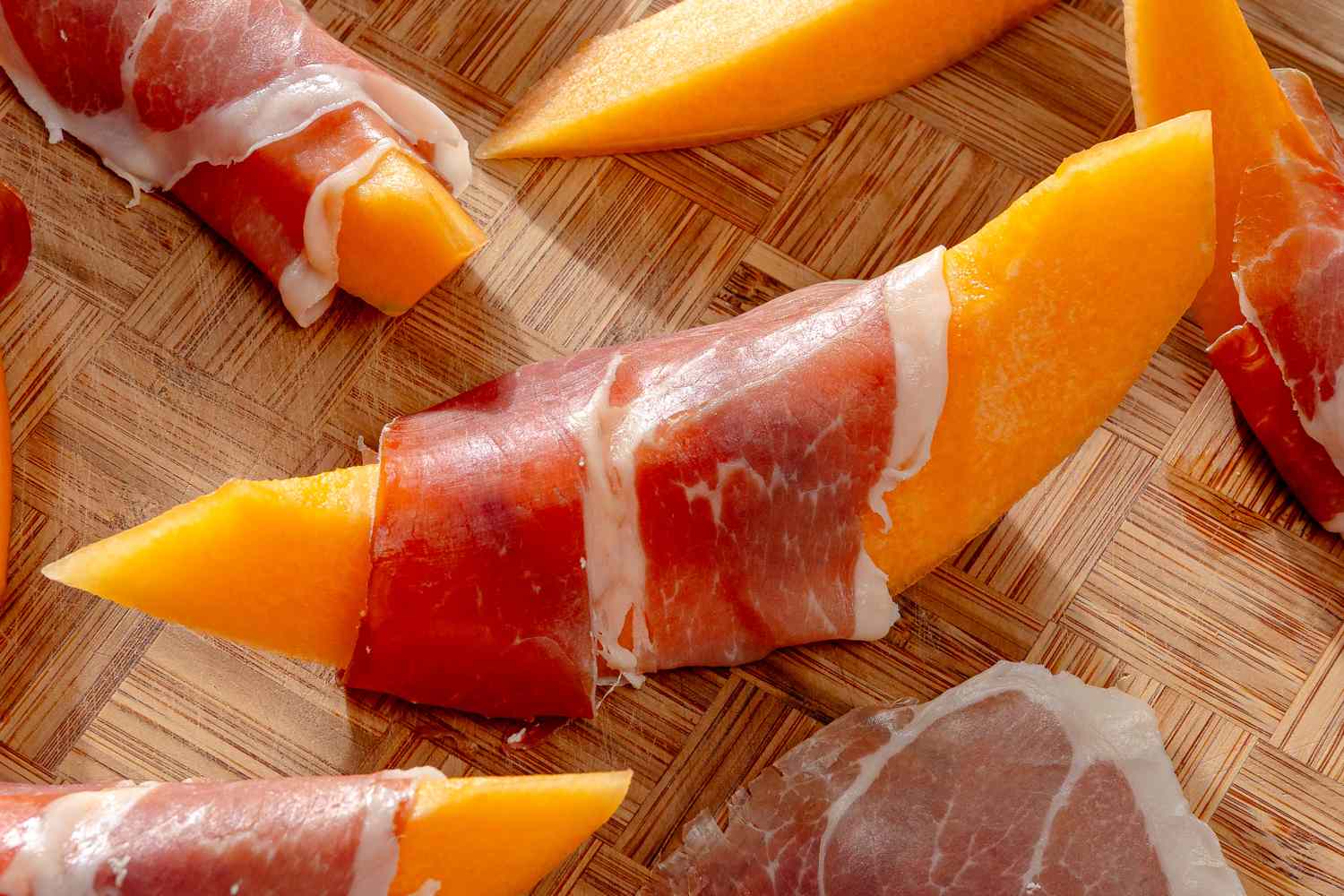 Slices of melon wrapped with thin pieces of prosciutto on a wooden surface