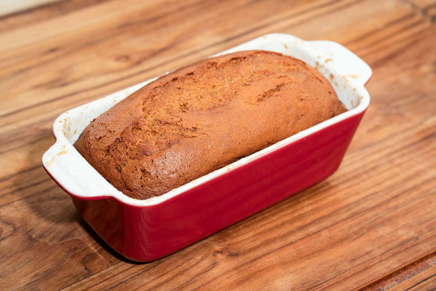 A loaf cake in a red baking dish on a wooden surface