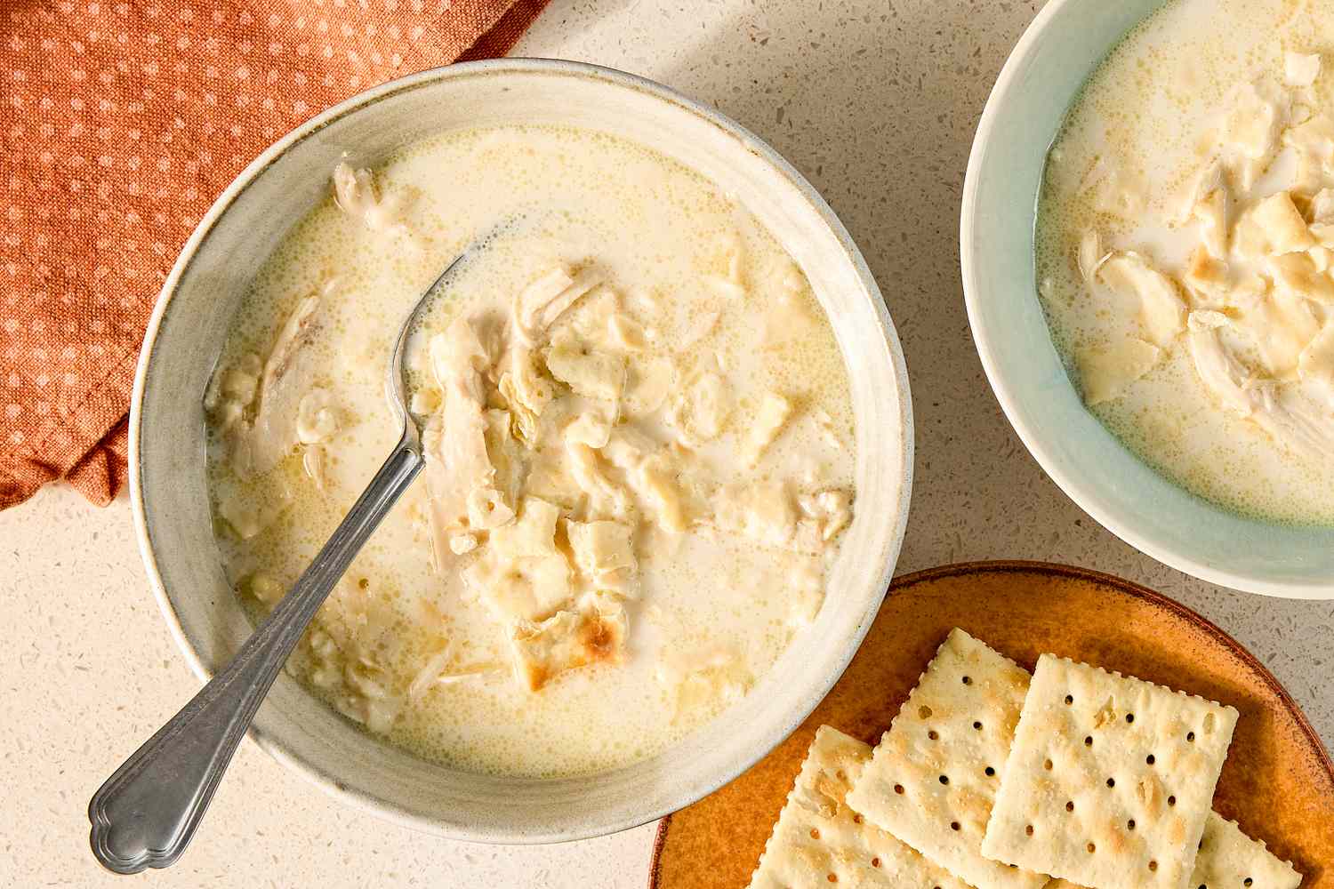 A bowl of chicken mull soup with a spoon accompanied by crackers on a plate