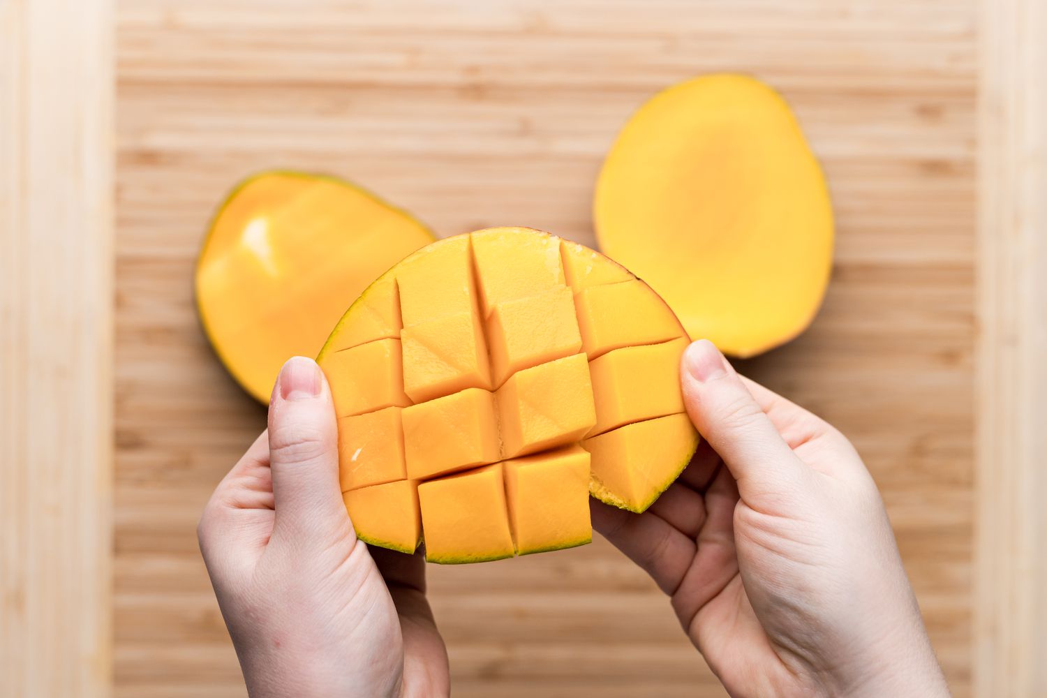 Pulling a slice of mango to show how to peel a mango.