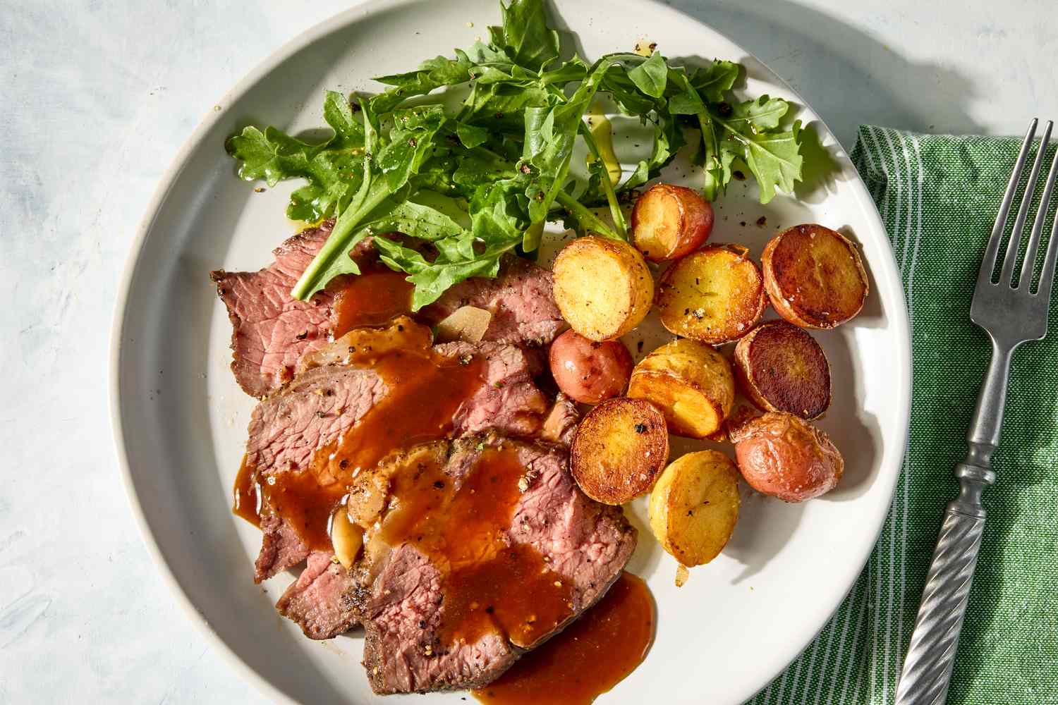 Plated roast beef slices with gravy roasted potatoes and arugula salad