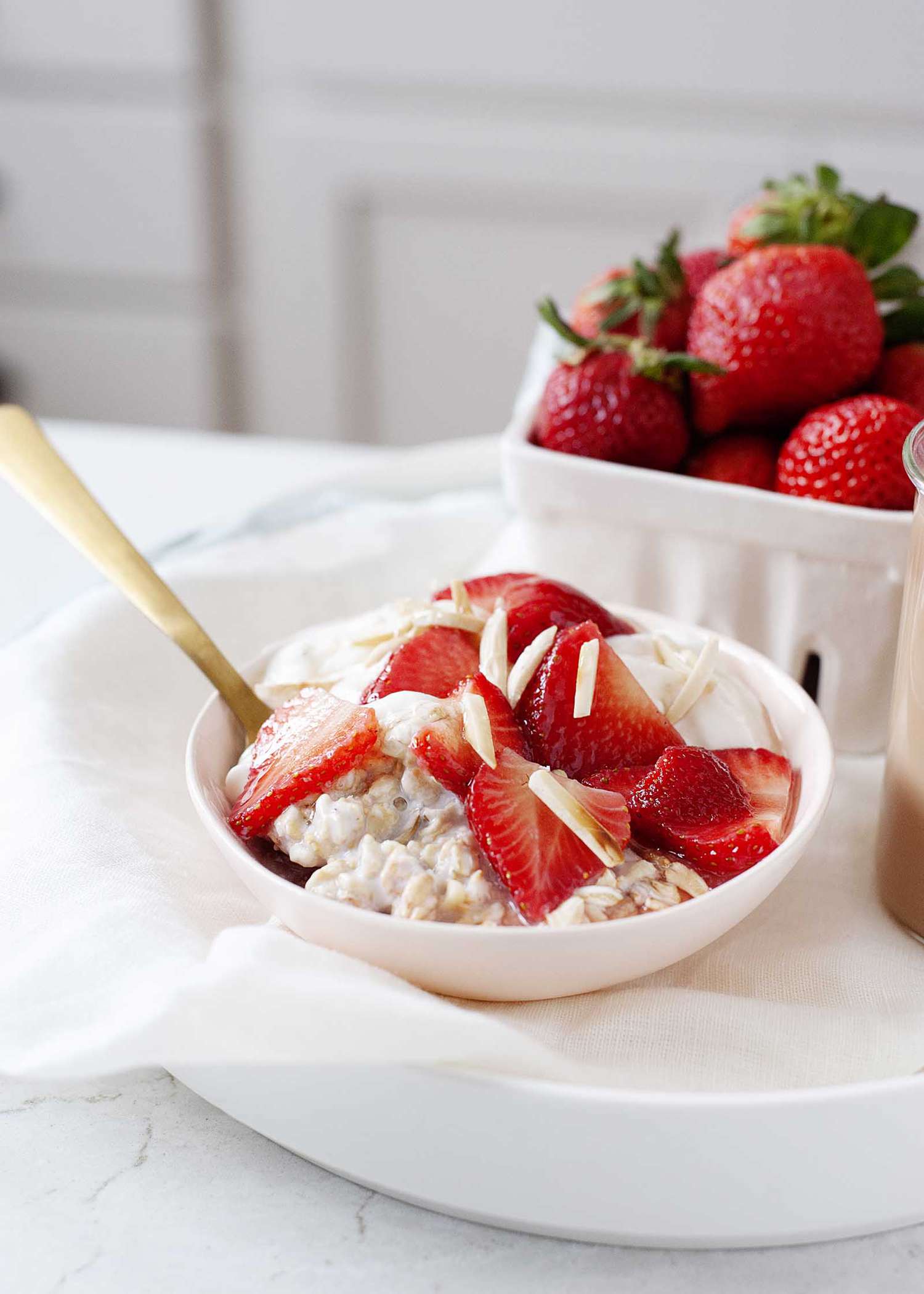 The best overnight oats topped with strawberries and sliced almonds with a gold spoon. A pint of strawberries is behind it.