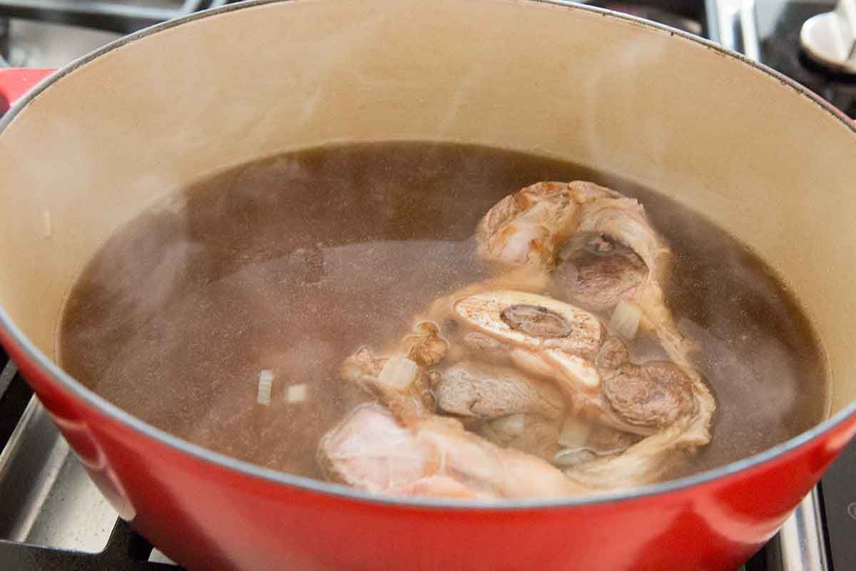 Beef shank simmering in broth in an oval Dutch oven