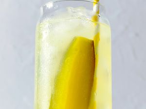 glass of iced lemonade with a pickle spear and a straw for Pickle Lemonade