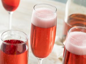 Fizzy pink cocktails in champagne flutes on a light wooden surface