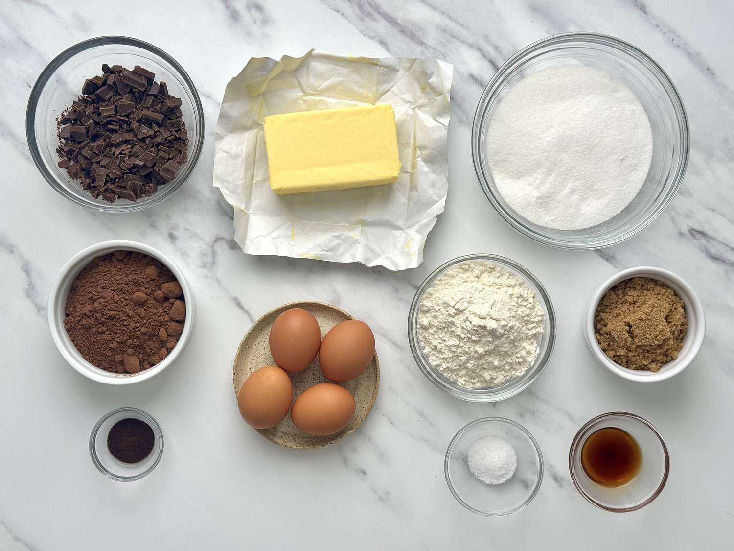Overhead shot of all brownie ingredients: chopped chocolate, cocoa powder, espresso powder, butter, eggs, flour, salt, vanilla, brown sugar, and granulated sugar