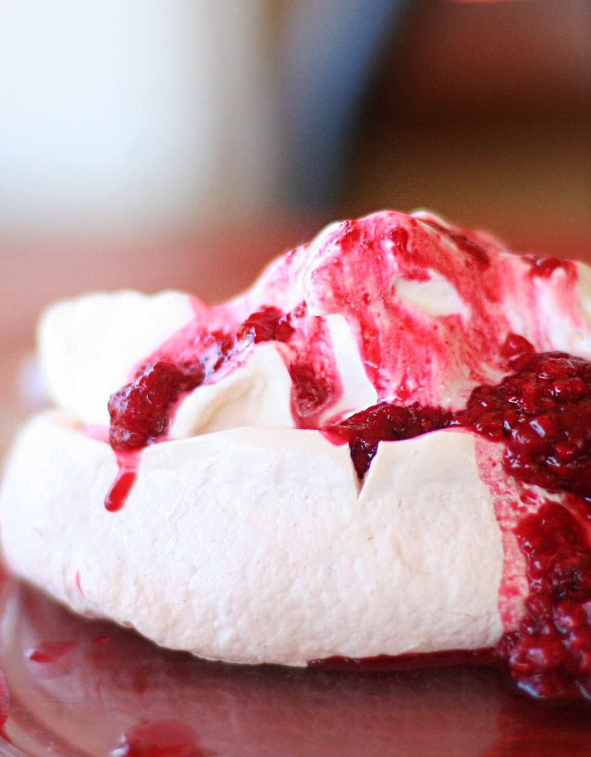 A pavlova dessert topped with whipped cream and raspberry sauce