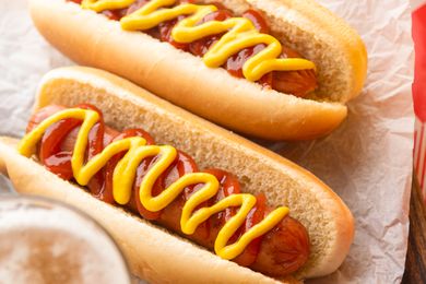 Two hot dogs in buns topped with ketchup and mustard, resting on parchment paper