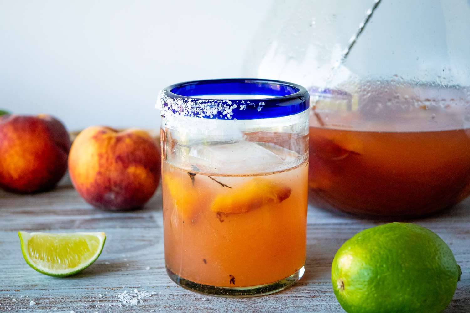 Grilled peach margarita on a table with limes and peaches.