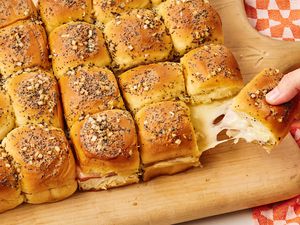Funeral Sandwiches on a serving board, one sandwich being pulled by a hand, delicious looking cheese stretch
