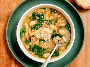 A white bowl with kale, white bean and sausage soup, places on a dark green plate on a wooden serving board