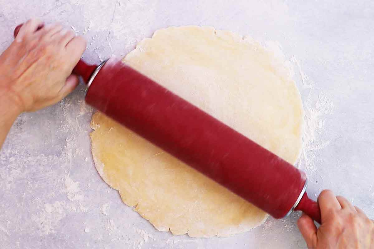 A pie dough is being rolled out on a floured surface with a rolling pin 