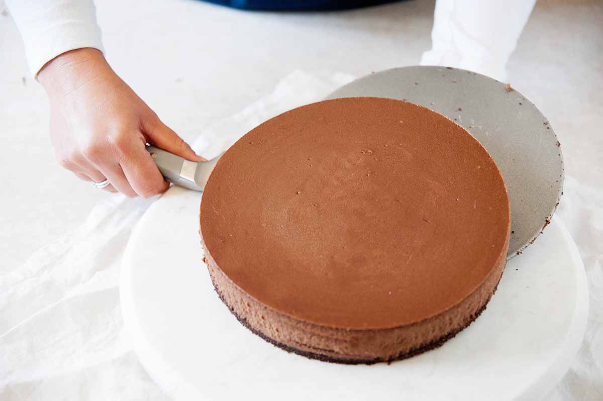 Carefully removing a cheesecake from the bottom of a cheesecake pan to transfer it to a marble cake plate.