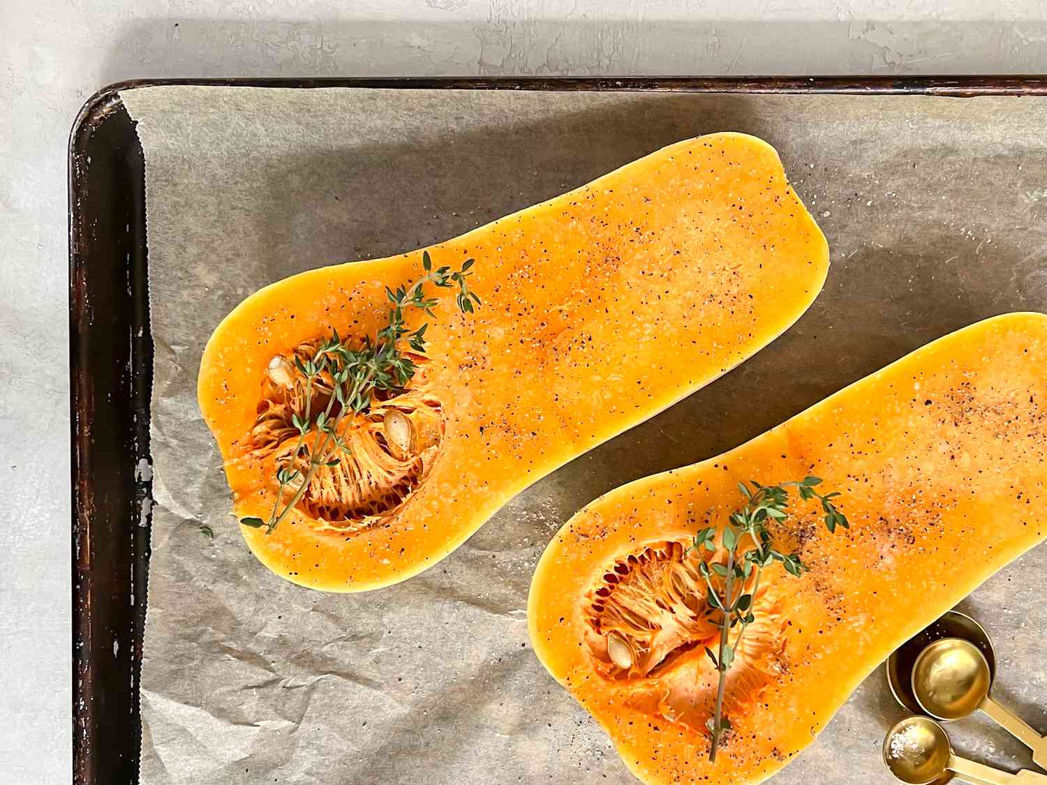 Butternut Squash (Flesh Side Up) Seasoned with Salt, Pepper, and Thyme Sprigs on a Lined Baking Pan 