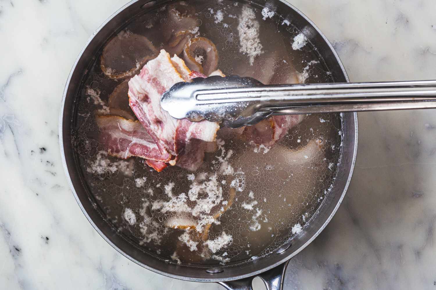 Adding bacon to a pot to make a coq au vin recipe.