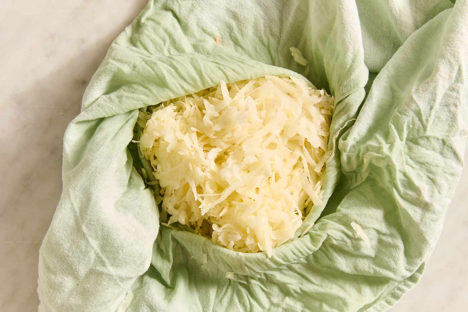 Overhead view of grated potatoes in a light green kitchen towel from Boxty (Irish Potato Pancakes) recipe