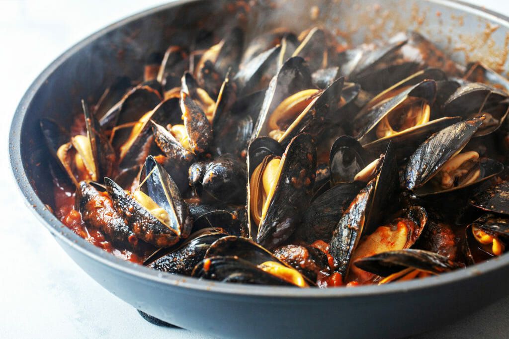 How to Cook Mussels in Tomato Sauce - closeup of steaming mussels in cast iron pan