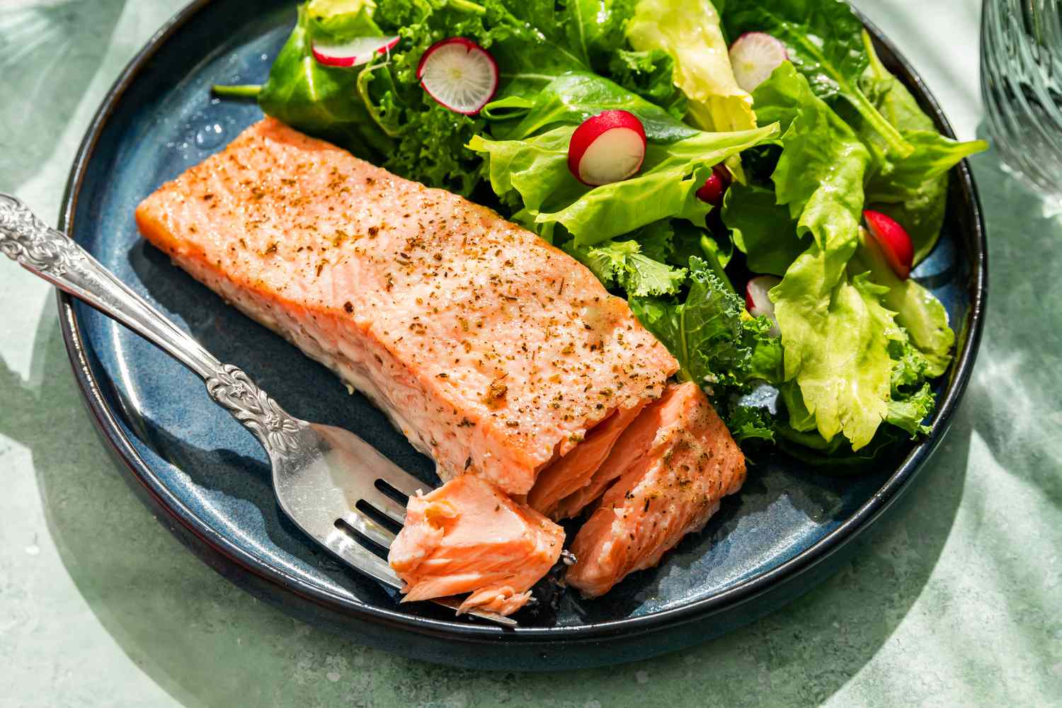 Mayo salmon fillet with a side green salad on a plate, with a fork having picked into one side of the salmon