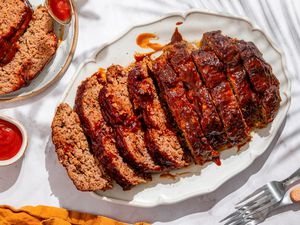 Overhead shot of 5-ingredient meatloaf (sliced) on a white serving plate, with two slices of meatloaf on another plate next to it
