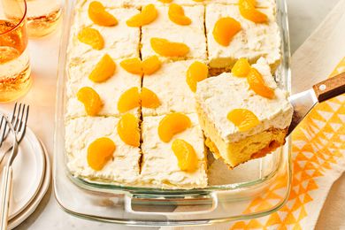 Angled view of a baking dish of pineapple and mandarin orange cake with a slice being removed with a spatula