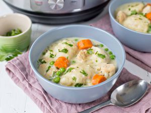 A blue bowl on a pink cloth filled with chicken and dumplings with an instant pot in the background.