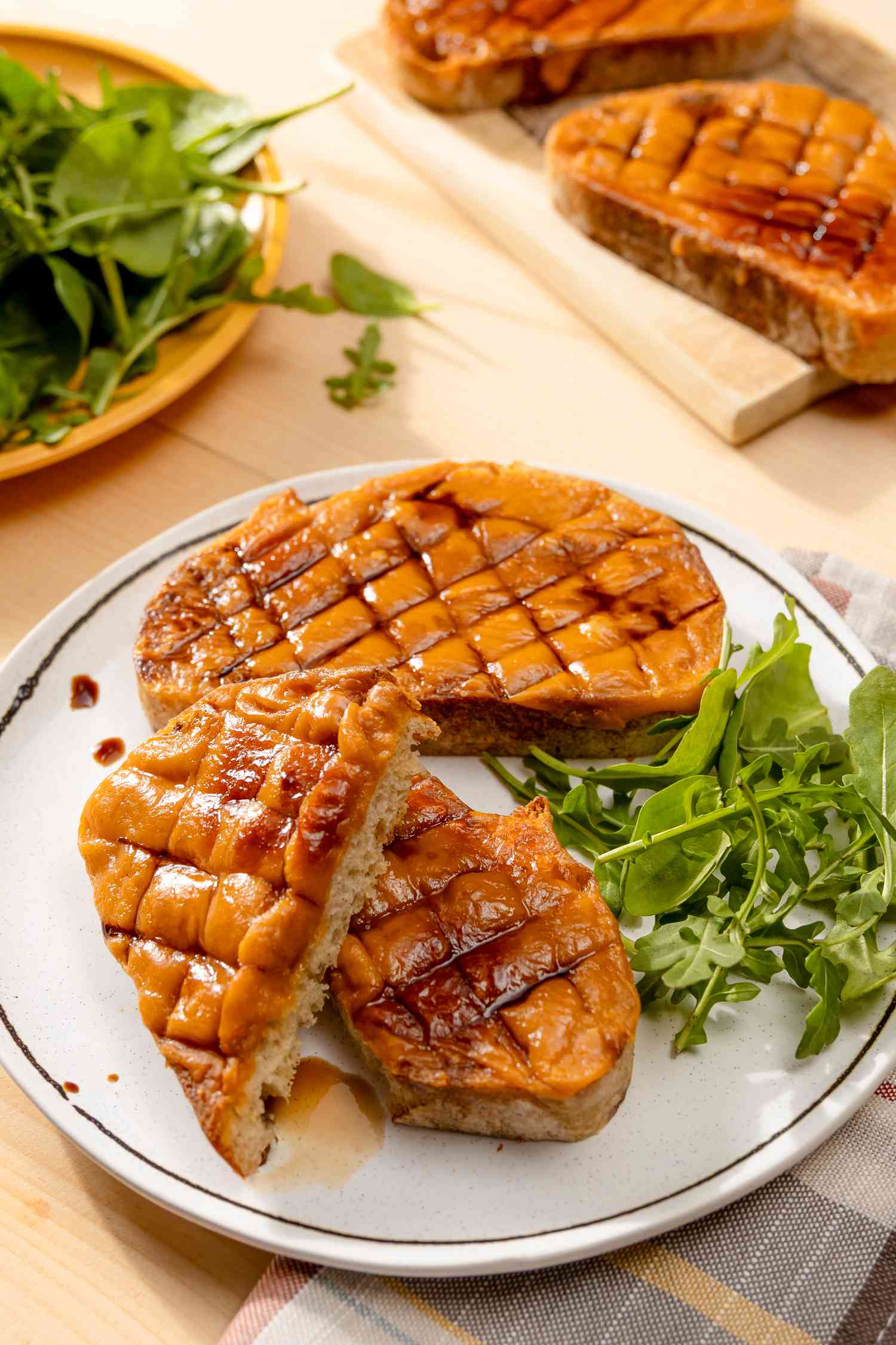 Serving of Welsh rarebit on plate with a side salad at a table with another serving on a plate and more welsh rarebit on a cutting board
