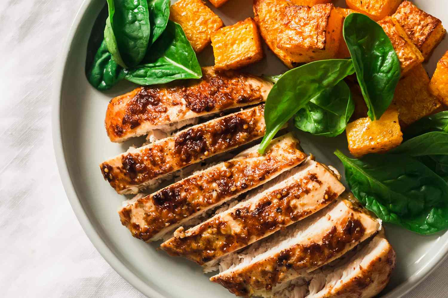 Overhead view of a plate roasted chicken breast, pumpkin and spinach on a light background