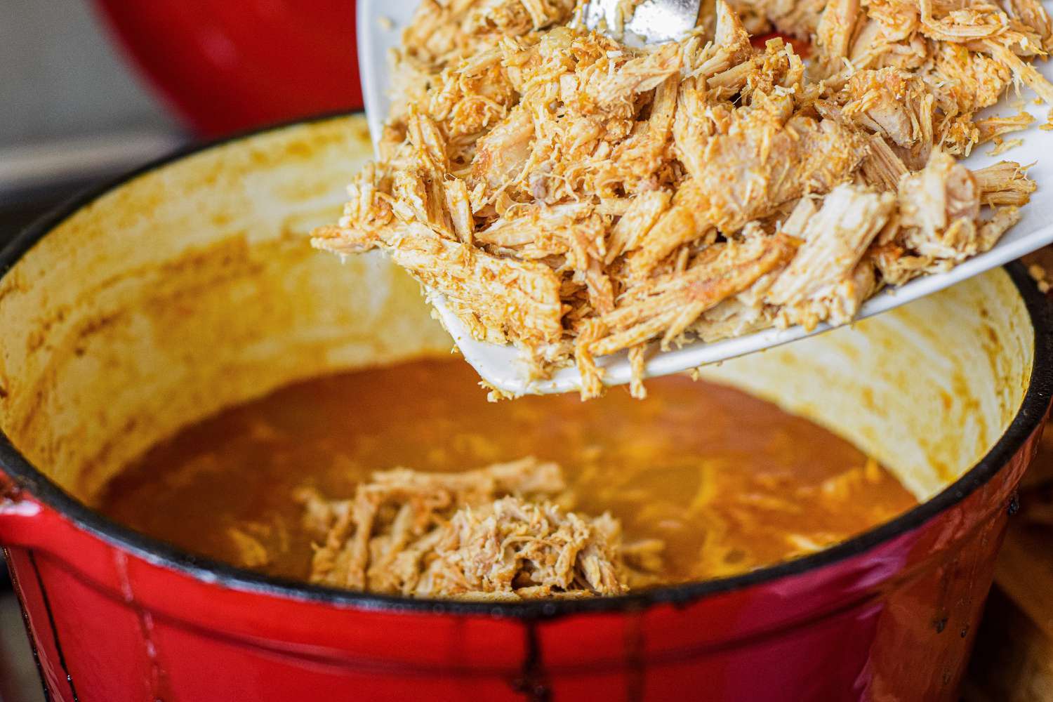 Shredded pork added to a dutch oven filled with sauce to make stove top pulled pork.