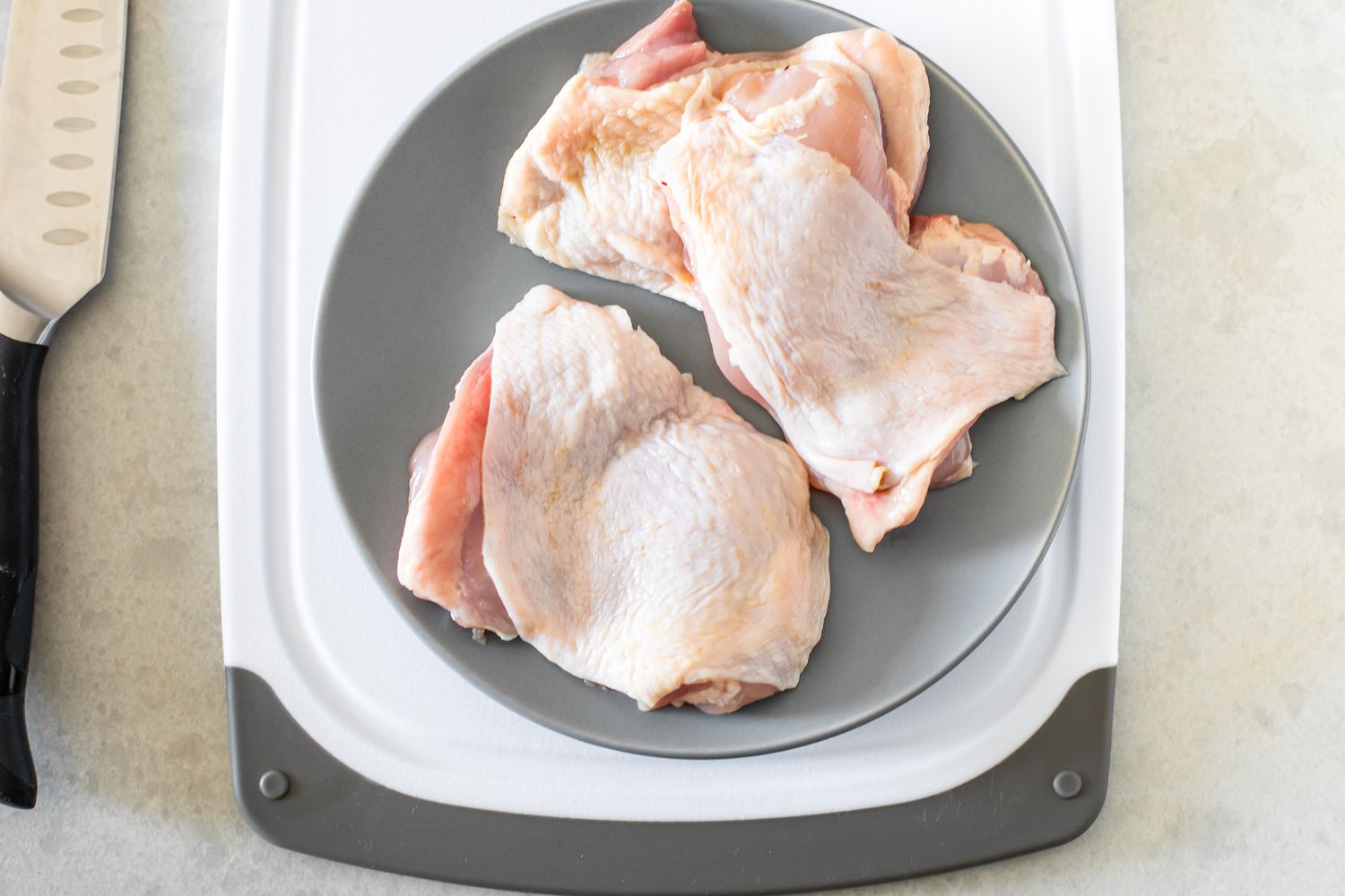 Plate of Boneless Chicken Thighs on a Cutting Board and on the Counter Next to It, a Knife