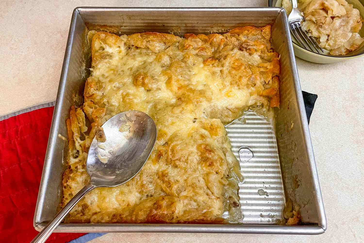 Baking Pan of Lay's 3-Ingredient Potato Chip Gratin With a Slice Cut Out and a Spoon. Next to the Pan, a Bowl With a Serving of the Gratin 