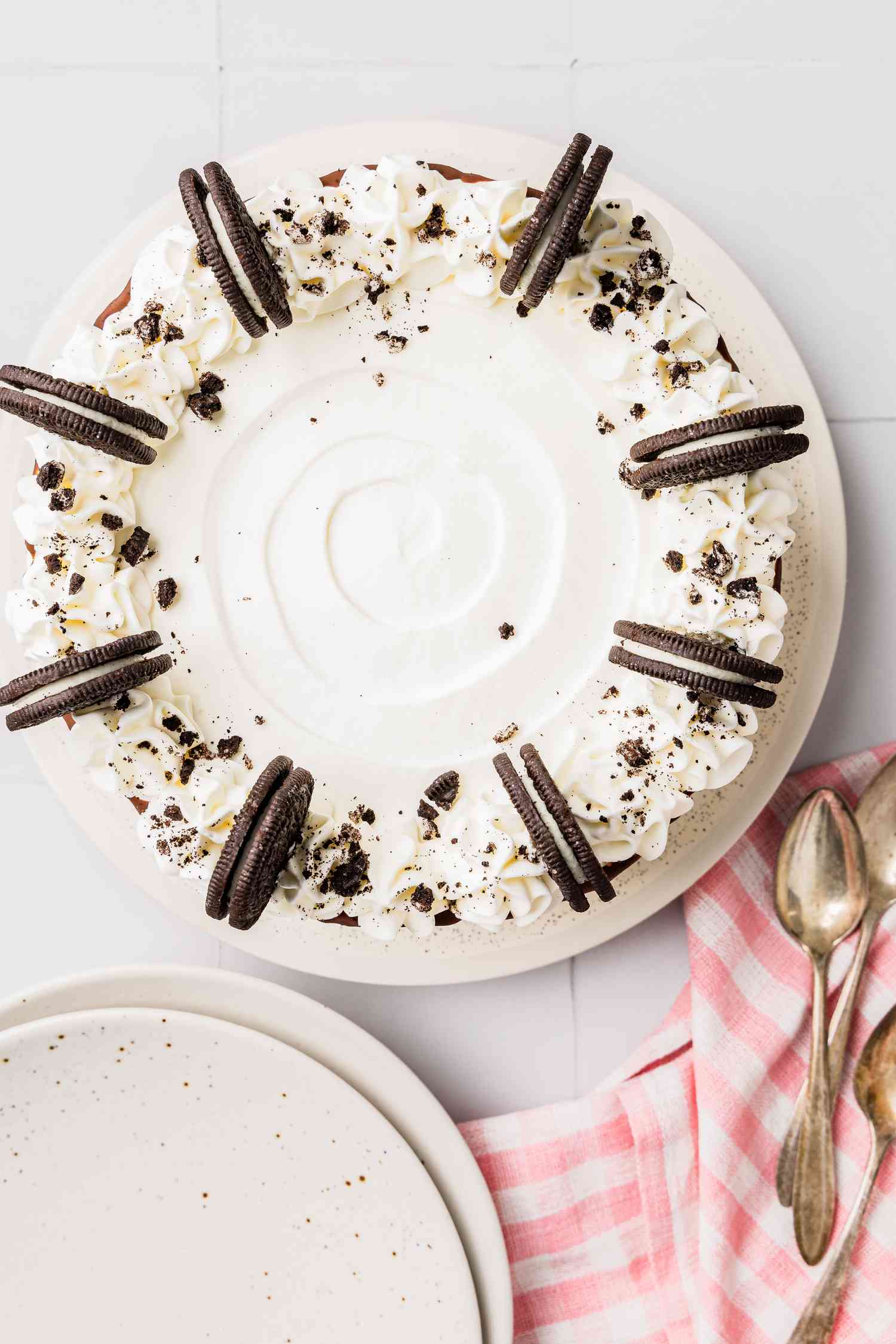 Plate of Oreo Ice Cream Cake and in the Surroundings, a Stack of Plates and Spoons on a Kitchen Towel 