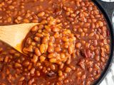 Baked beans in a cast iron skillet with a wooden spoon