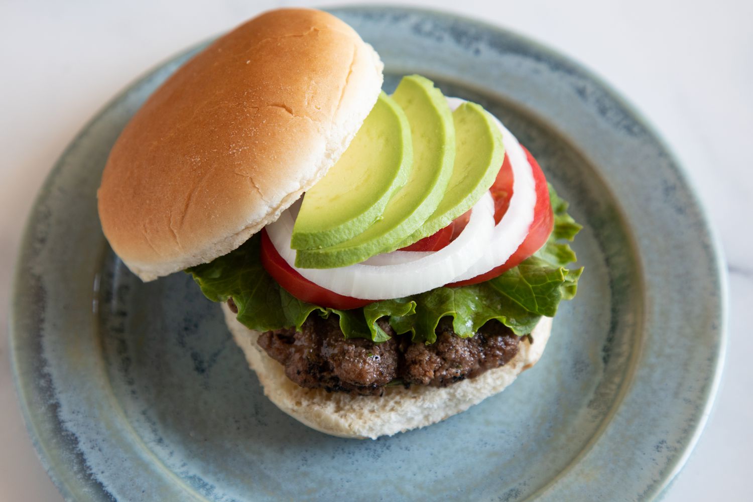 A famous burger topped with avocado on a plate.